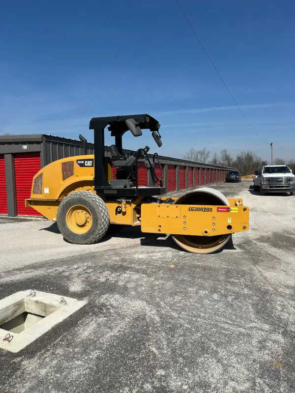 CAT soil compactor parked on construction site near storage units under clear blue sky.